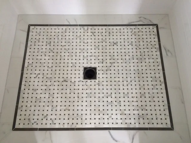 Shower floor of marble basketweave mosaic with a dark border and a square drain