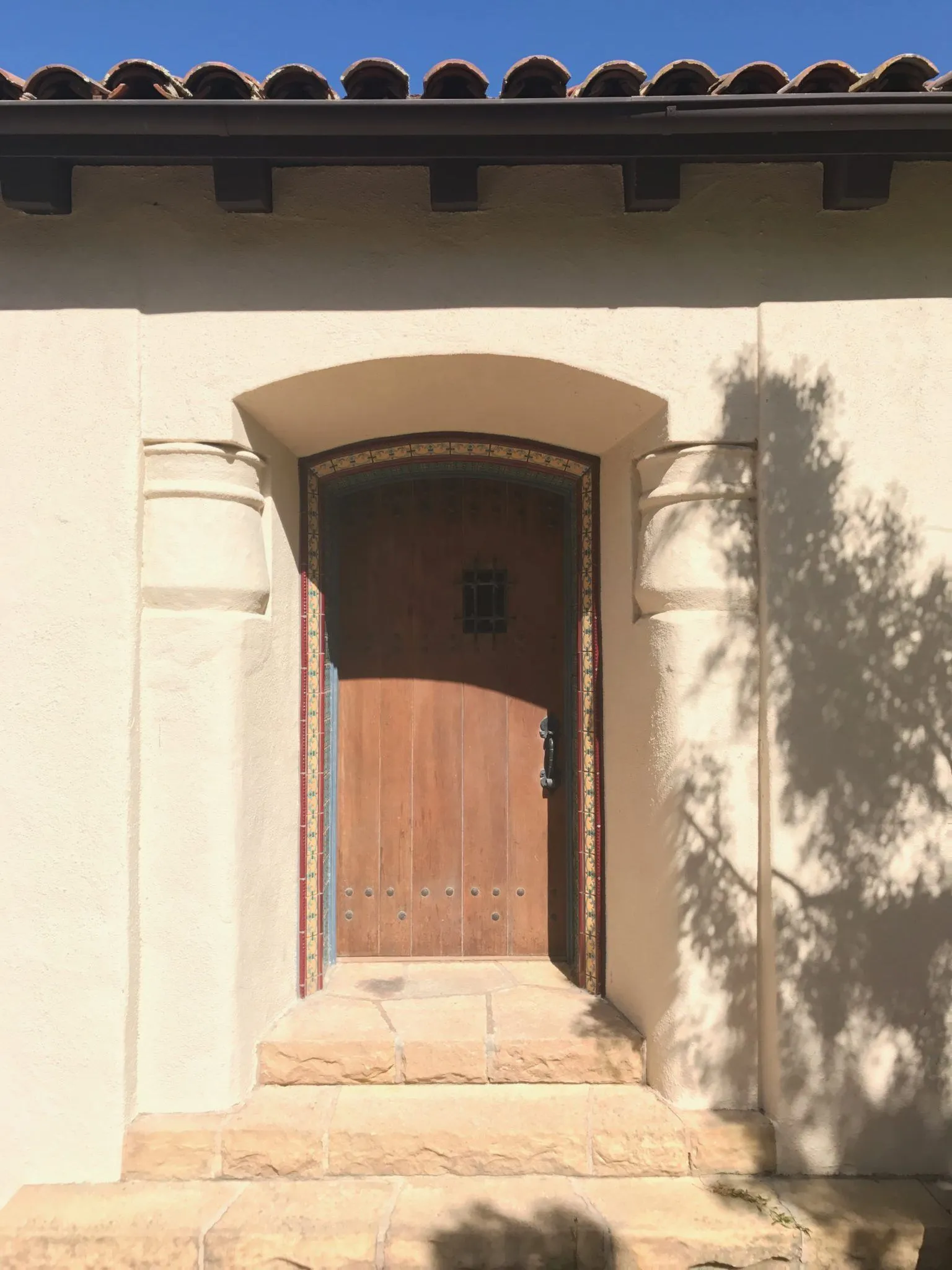Spanish-style front entry with tiled steps and a decorative tile border around an arched wood door