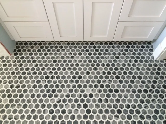 Gray and white hexagon mosaic bathroom floor in front of white cabinets