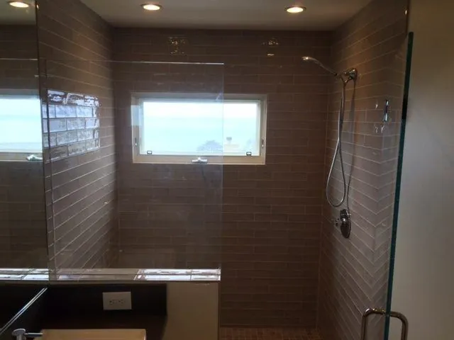 Walk-in shower in gray glass subway tile with an ocean-view window and a glass panel