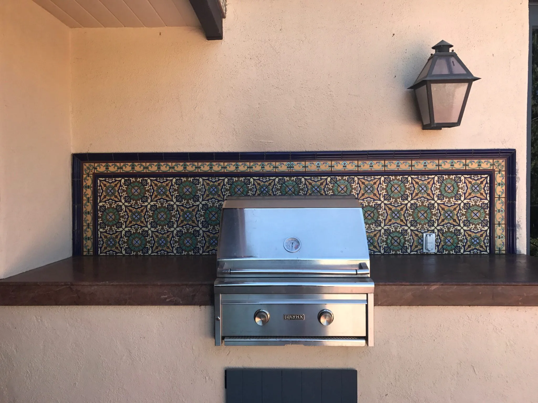Outdoor kitchen with a blue and gold Spanish tile backsplash behind a built-in grill