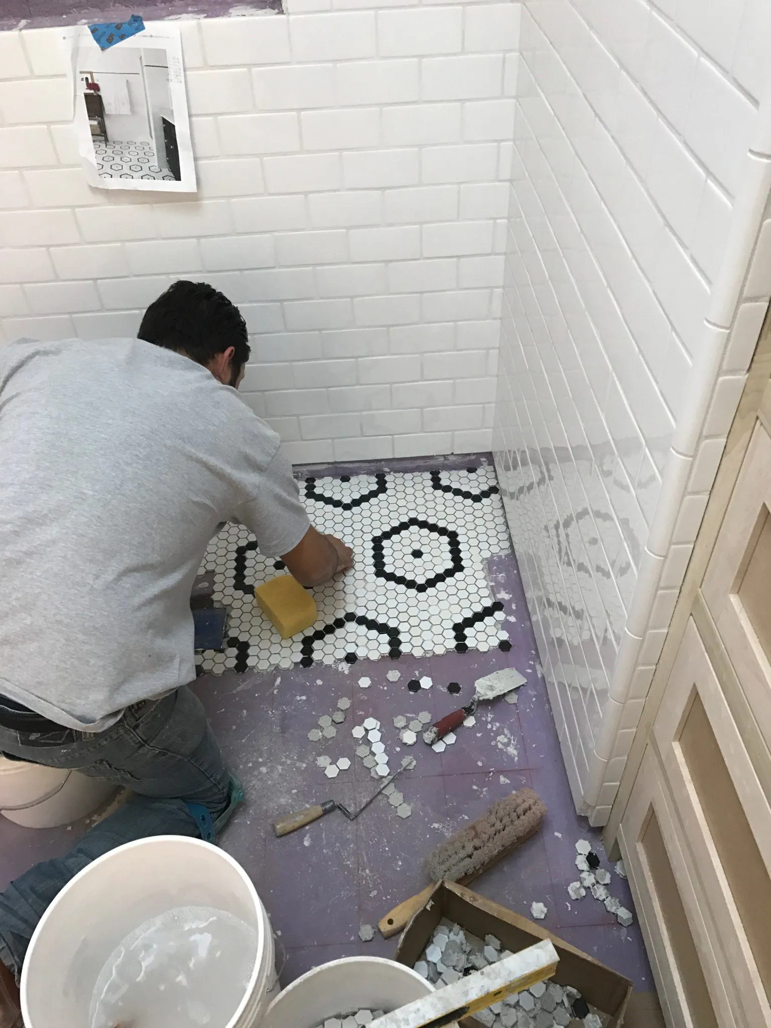 Tile setter installing a black and white hexagon mosaic floor in a white subway-tile shower